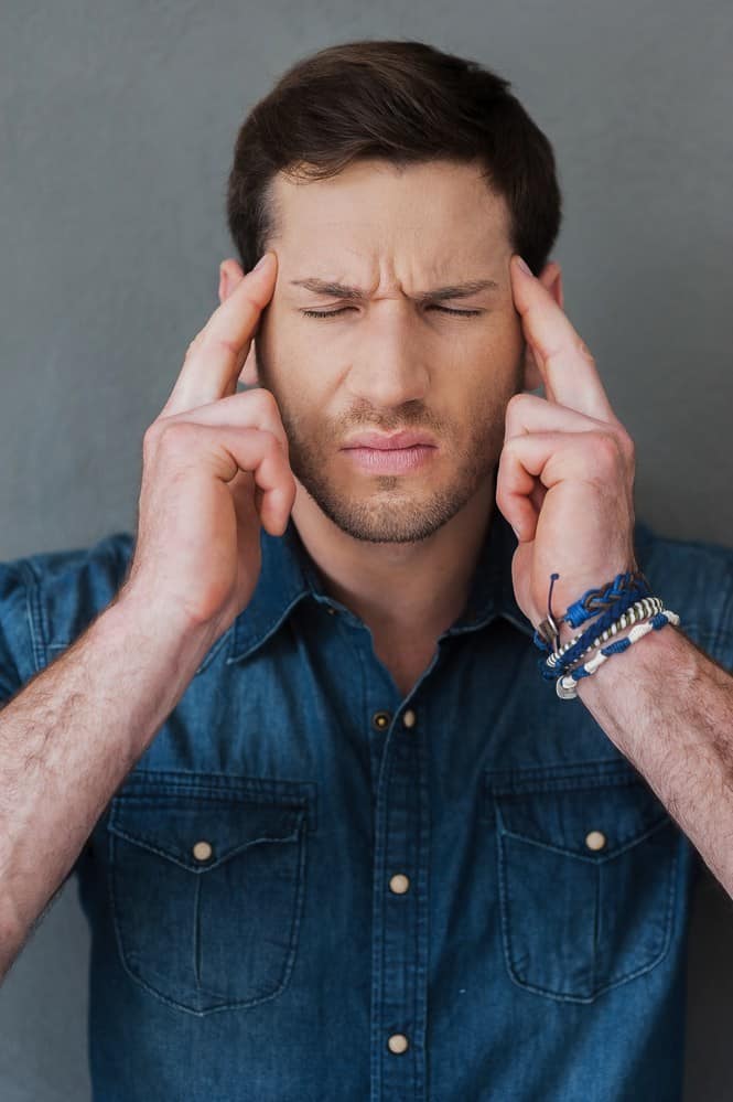 Feeling exhausted. Frustrated young man touching his head while standing against grey background